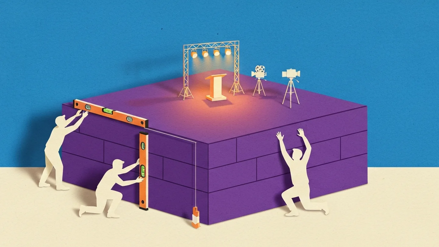 A massive block base taking up most of the frame with a small lit stage, podium and cameras on top of it, while three figures work at the base itself with spirit levels and a plumb line