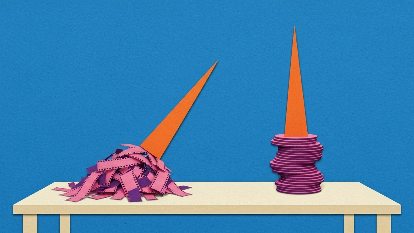 Two identical orange spires standing on a table. The left one is driven into a loose heap of shredded film and leans over. The right one stands straight on a stacked, solid base